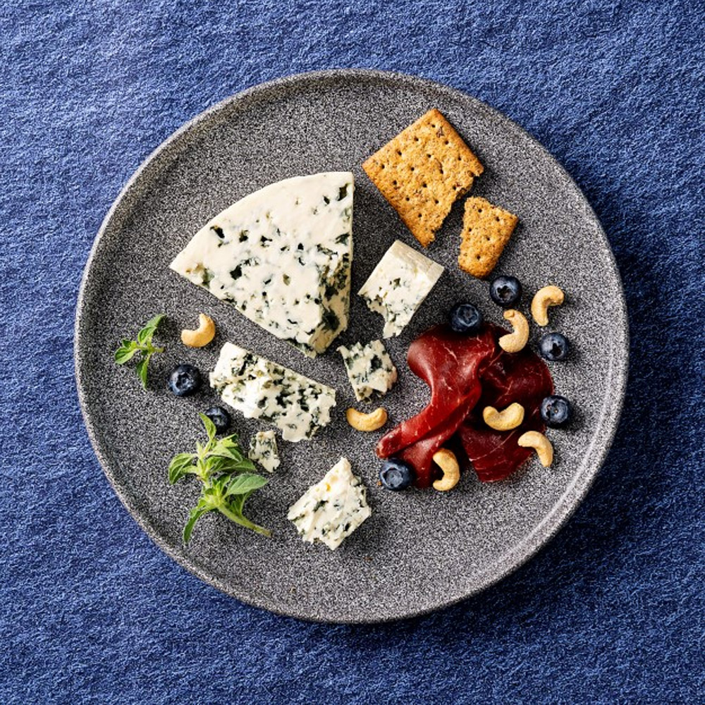 A wedge of Castello Extra Creamy Blue Cheese on a plate with other snacks