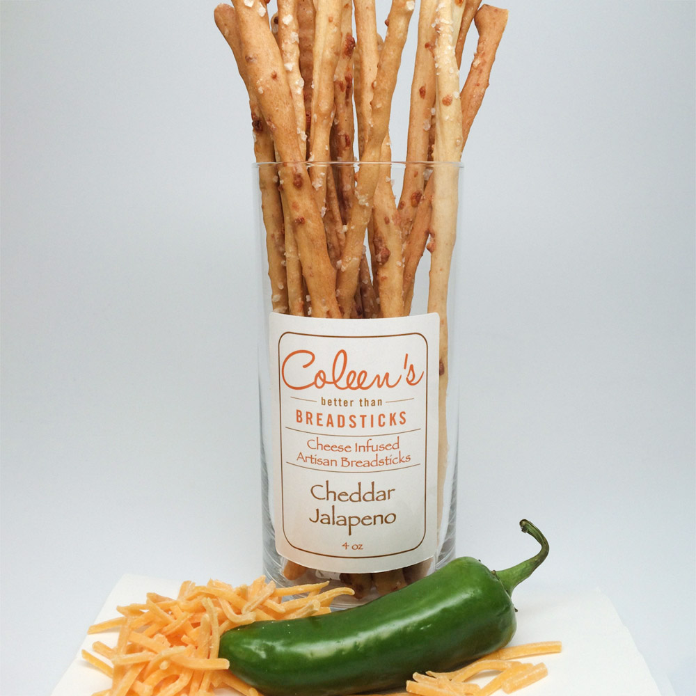 Coleen's cheddar jalapeno breadsticks in a glass container on a plate with shredded cheese and a jalapeno