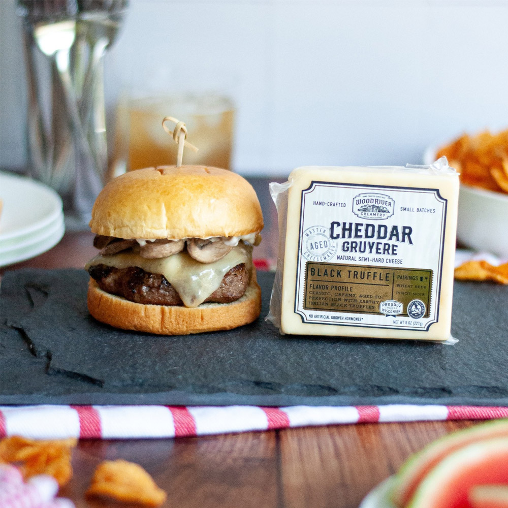 A burger with cheese and mushrooms next to Wood River Creamery Black Truffle Cheddar Gruyere in its packaging