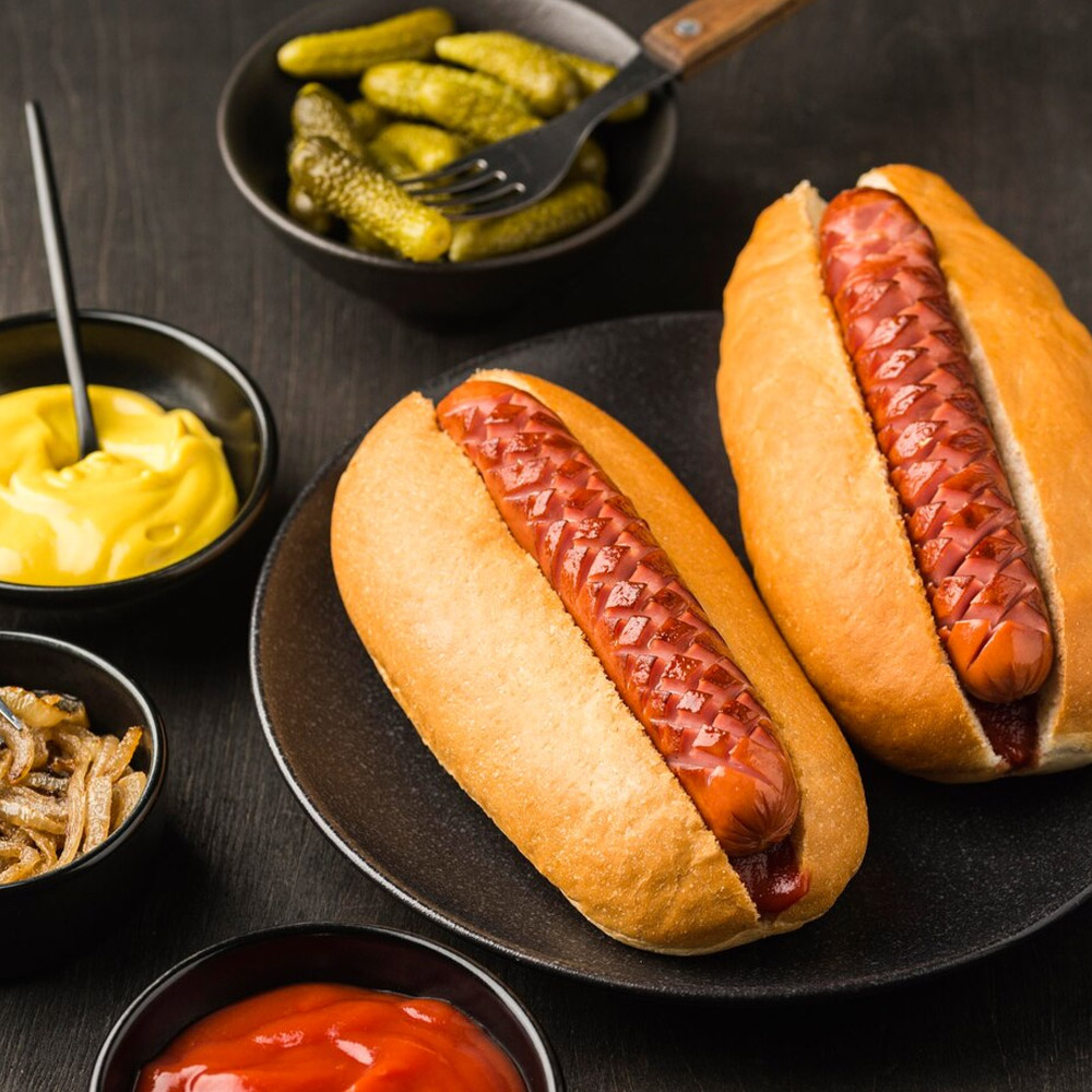 Hot dogs in buns next to bowls of hot dog condiments