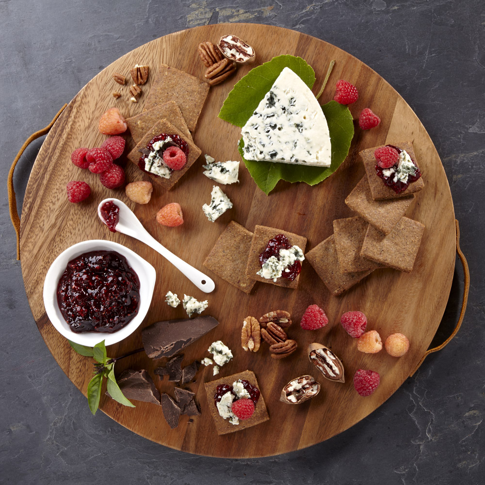 Castello Danish blue cheese on a wooden board with berries, crackers, jam, chocolate and nuts