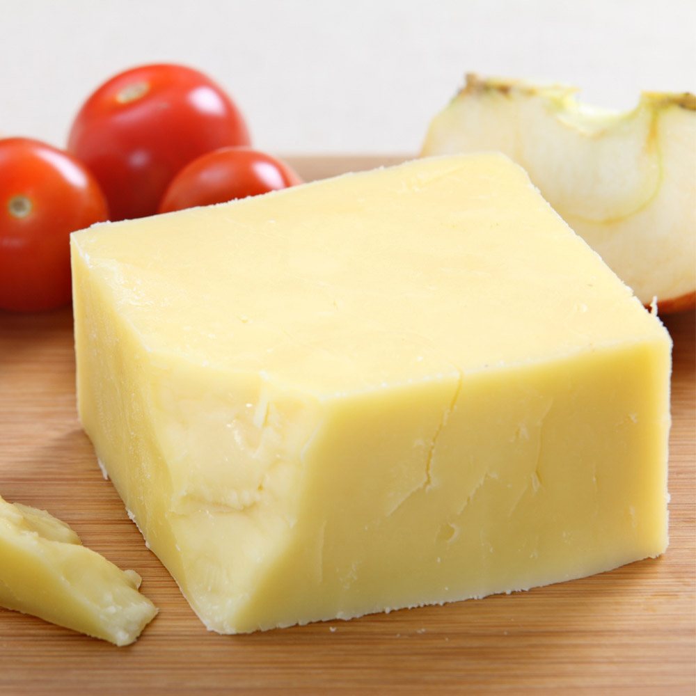 A block of white cheddar cheese on a wood board with tomatoes in the background