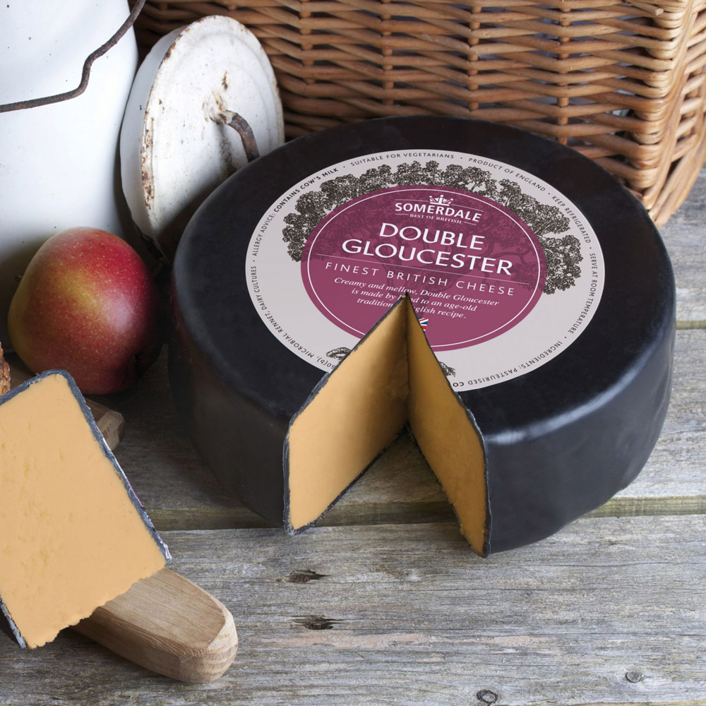 Wheel of Somerdale double Gloucester cheese next to an apple and a picnic basket