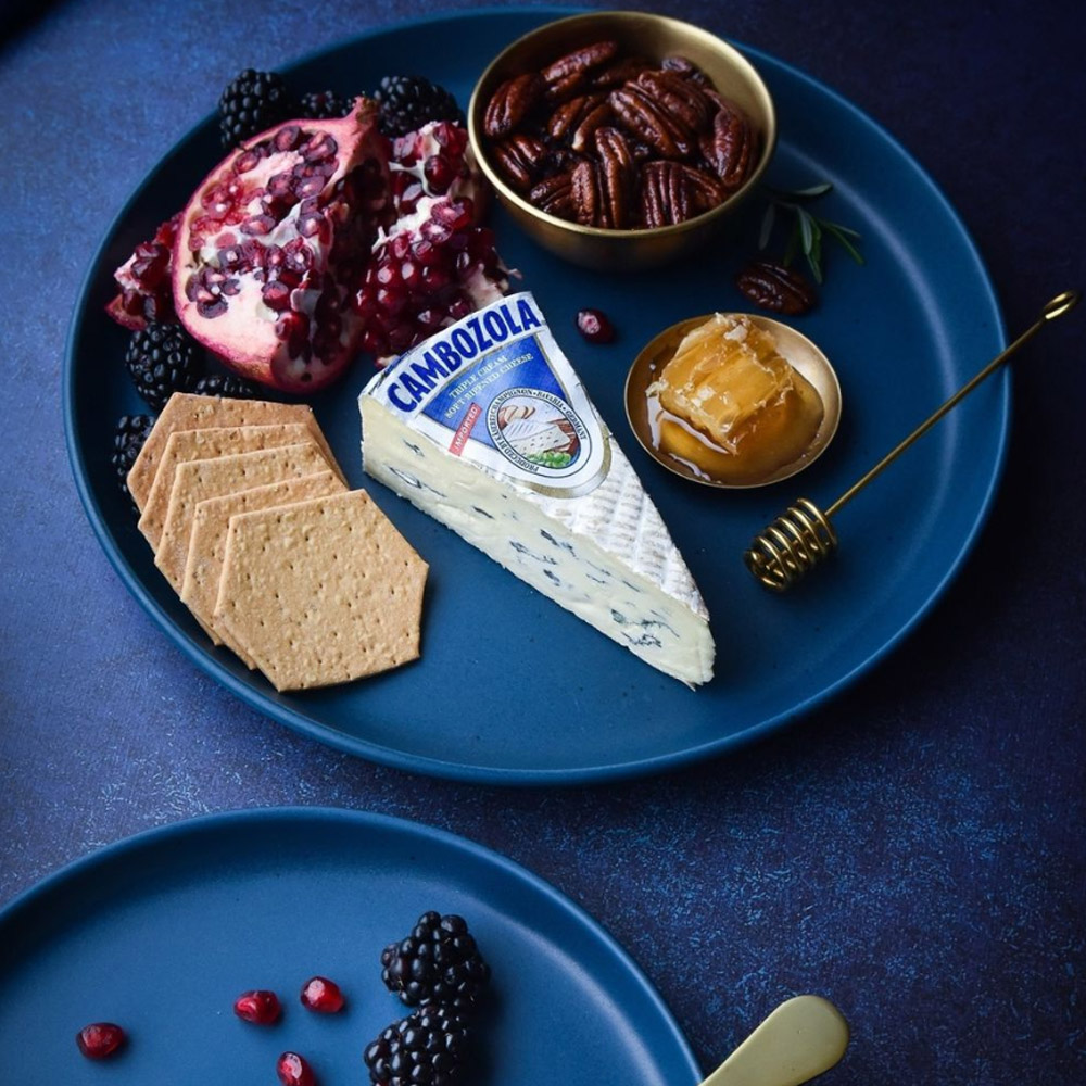 A wedge of Cambozola cheese on a plate with crackers nuts and fruit