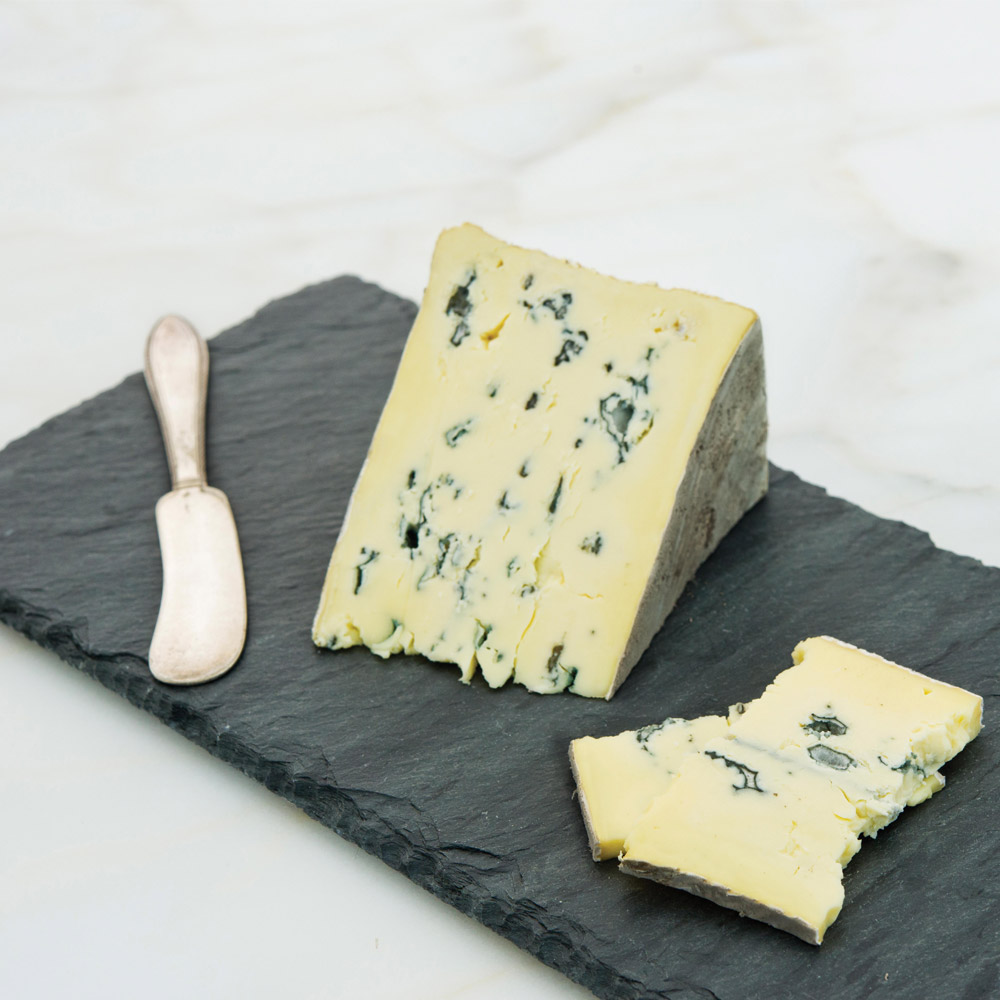 Wedge of Cambozola black label blue cheese on a slate board with a cheese knife