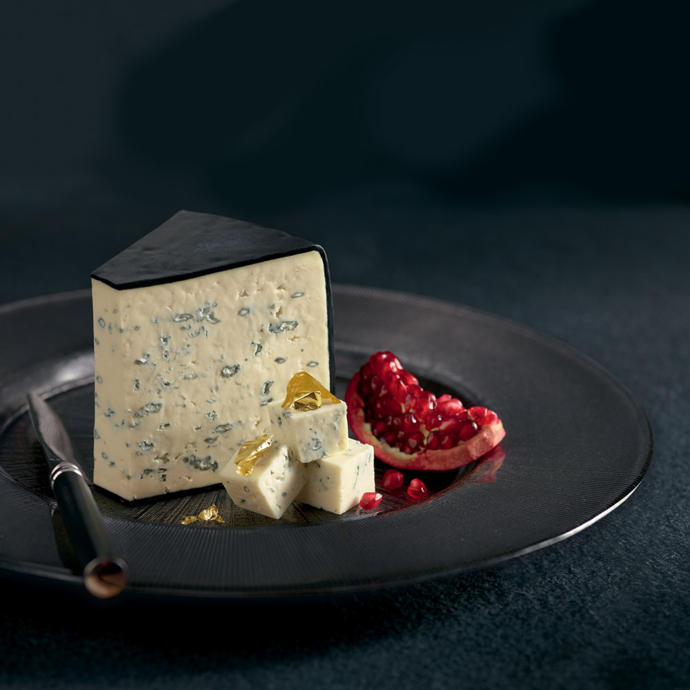 Wedge of Grand Noir blue cheese on a plate with honey and pomegranate and a cheese knife