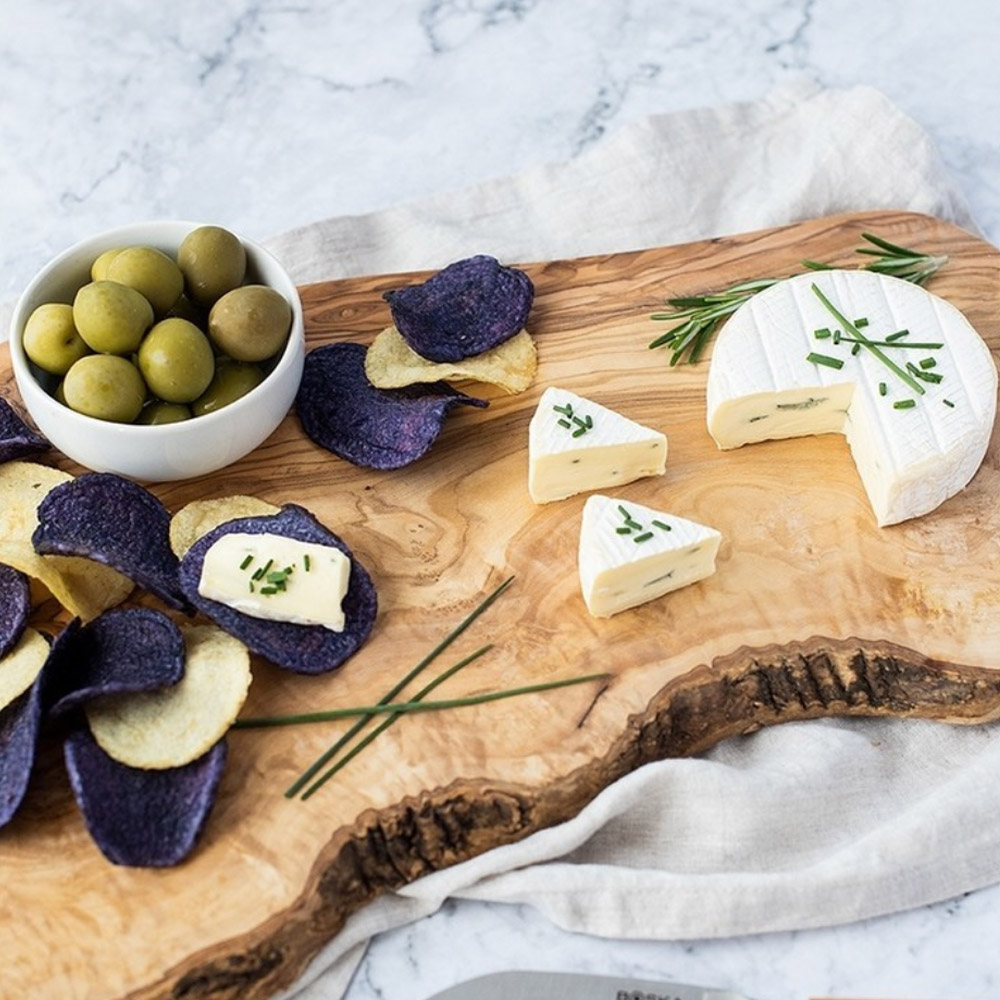 Brie on a wood board with a bowl of olives and potato chips