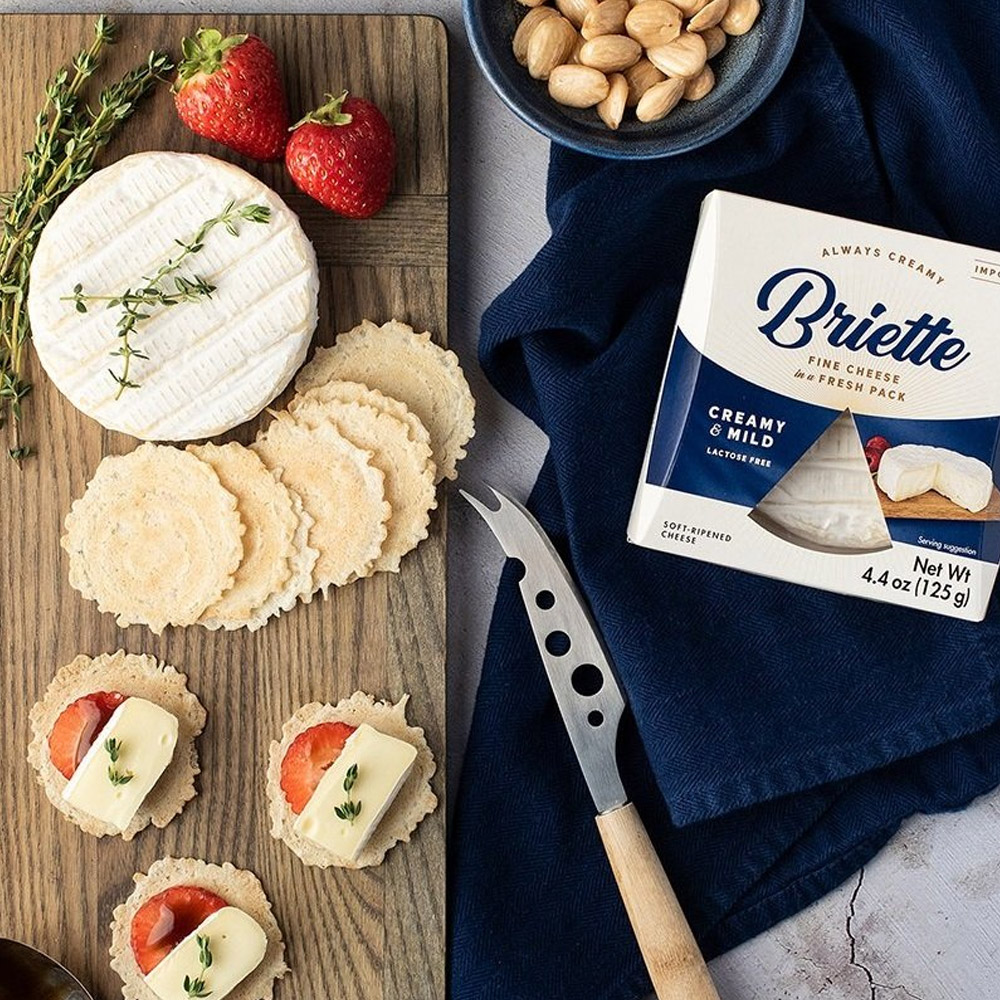 A package of Briette Creamy & Mild next to a cheese board with crackers and strawberries