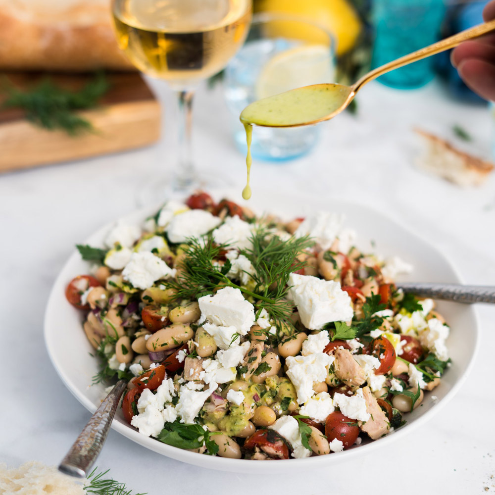 Mt Vikos barrel aged feta cheese sprinkled on a salad in a bowl next to a wine glass