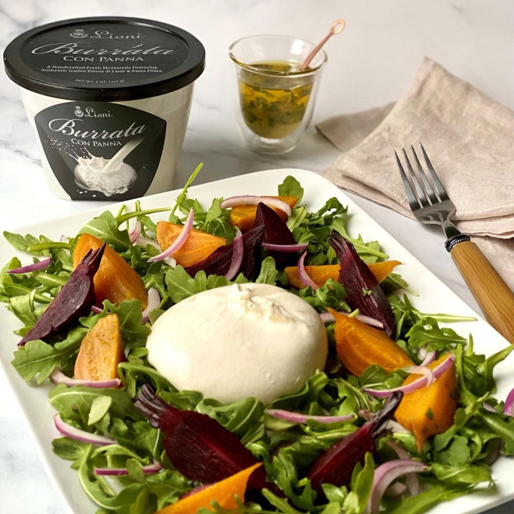 A salad topped with burrata in front of a Lioni burrata container