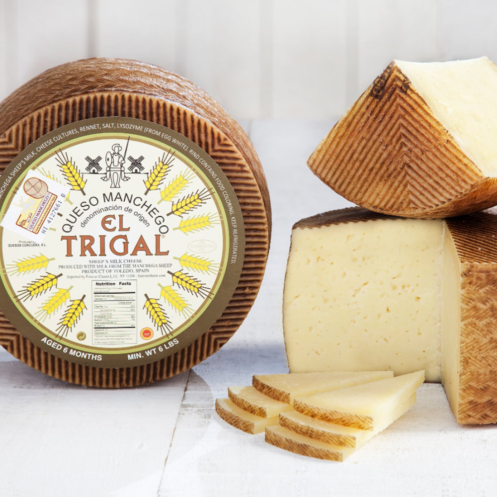 Wheel of El Trigal 6 month Manchego DOP cheese next to a cut wheel of manchego cheese