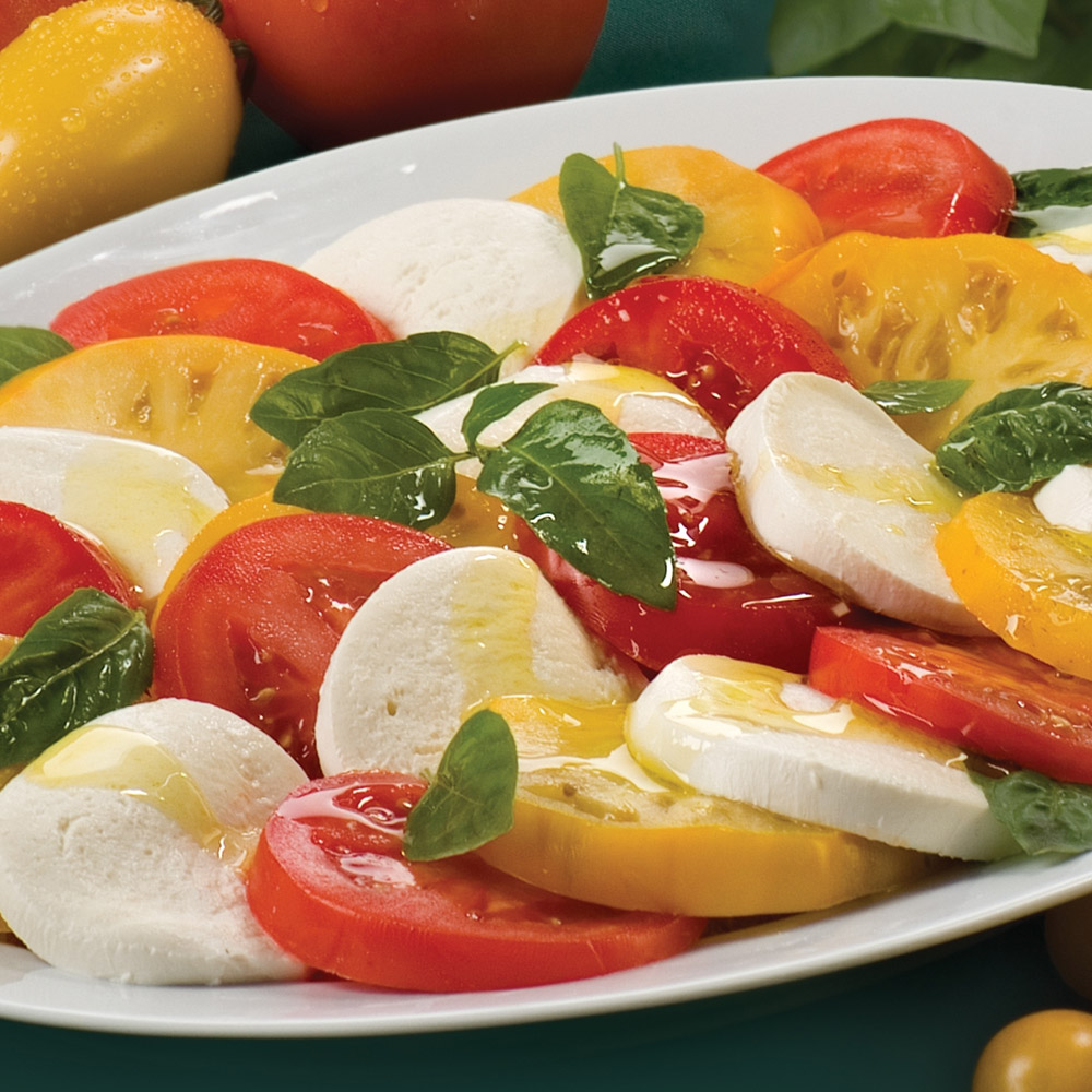A close-up of a fresh mozzarella and tomato Caprese salad with red and yellow tomatoes and fresh basil leaves
