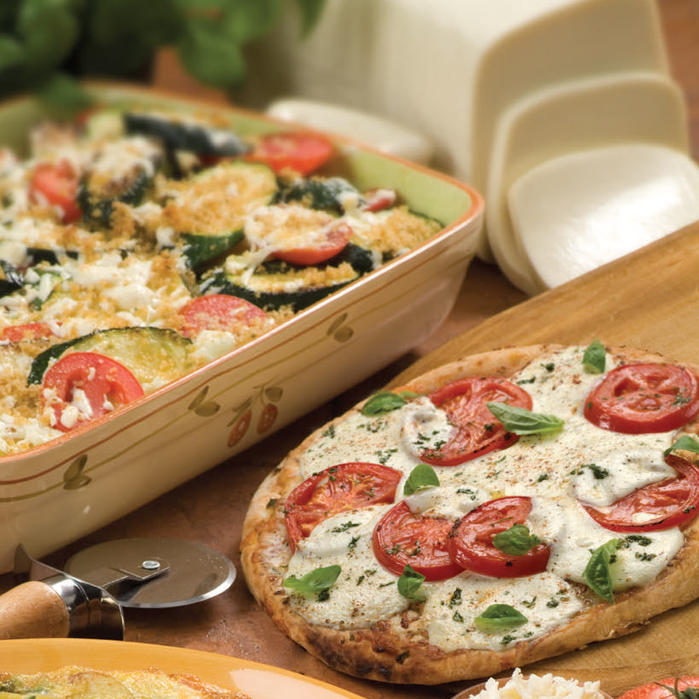 A pizza next to a vegetable casserole that is next to a sliced mozzarella loaf
