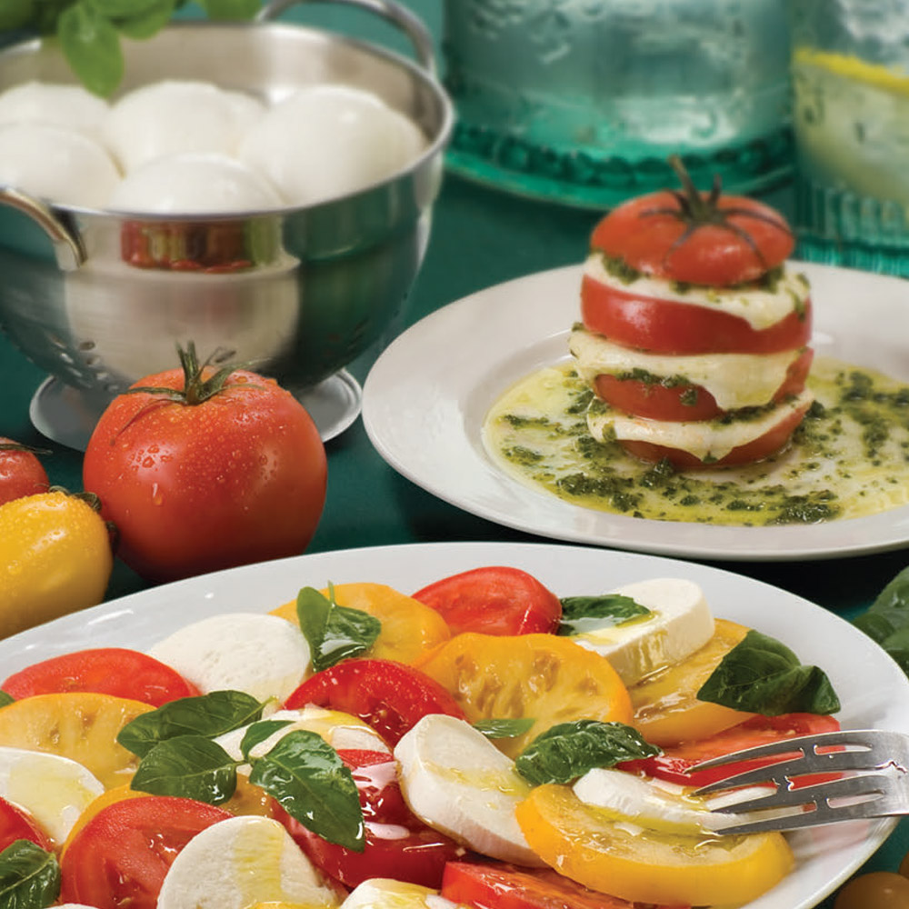 A Caprese salad on a plate in front of a bowl of ovoline fresh mozzarella