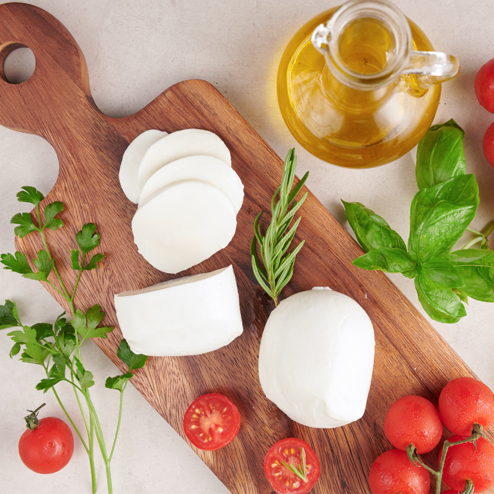 Buffalo mozzarella on a cutting board with tomatoes and herbs next to a bottle of olive oil