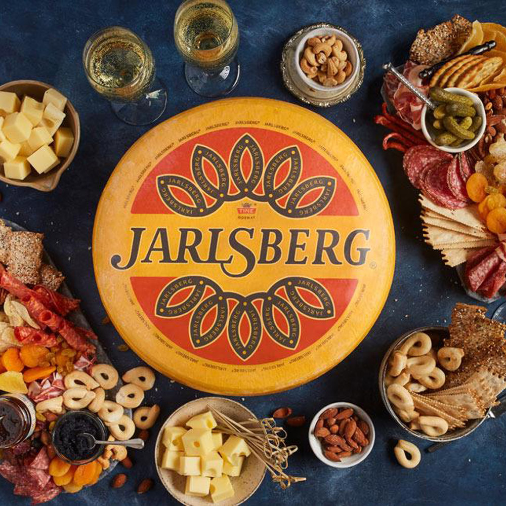 A wheel of Jarlsberg Swiss cheese on a cheese board surrounded by snacks and wine