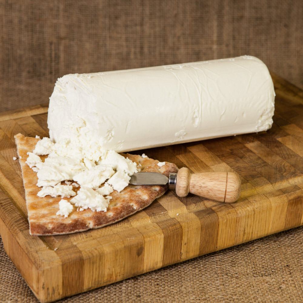 Log of Mitica Capricho de Cabra cheese on a cheese board with pita bread and a cheese knife