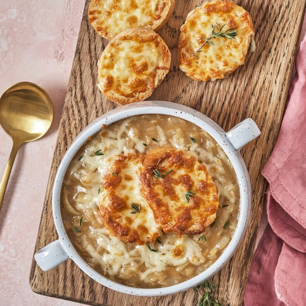 A bowl of French onion soup topped with cheese next to a gold spoon and three bread pieces topped with cheese