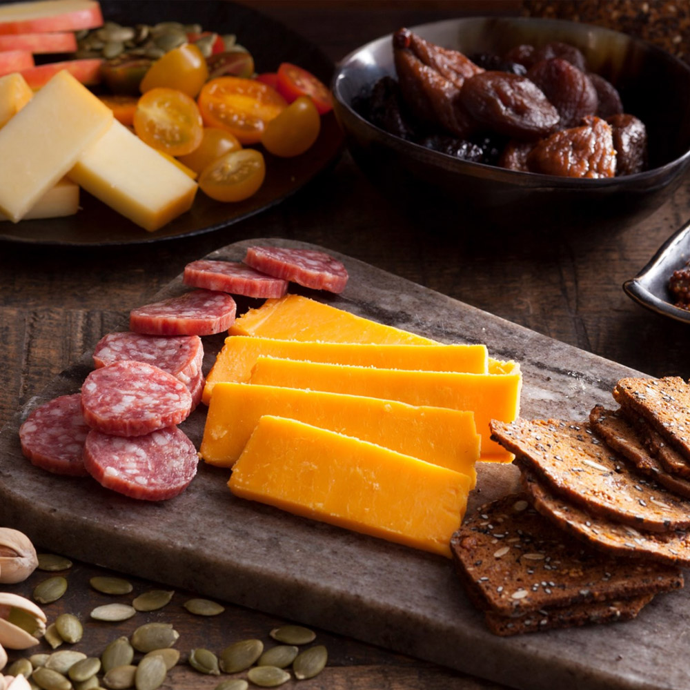 A cheese board with yellow cheddar and salami with crackers