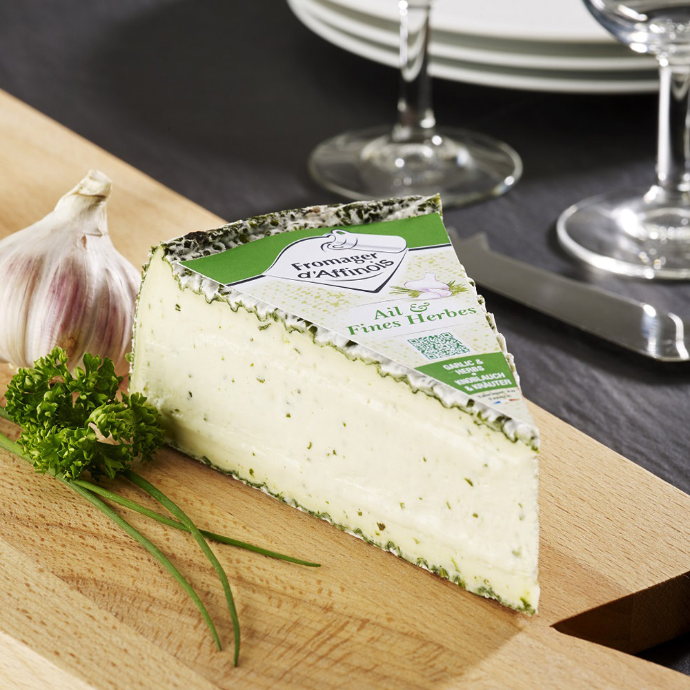 Wedge of Fromager D'affinois cheese with Garlic and Herbs on a wood board with garlic and herbs