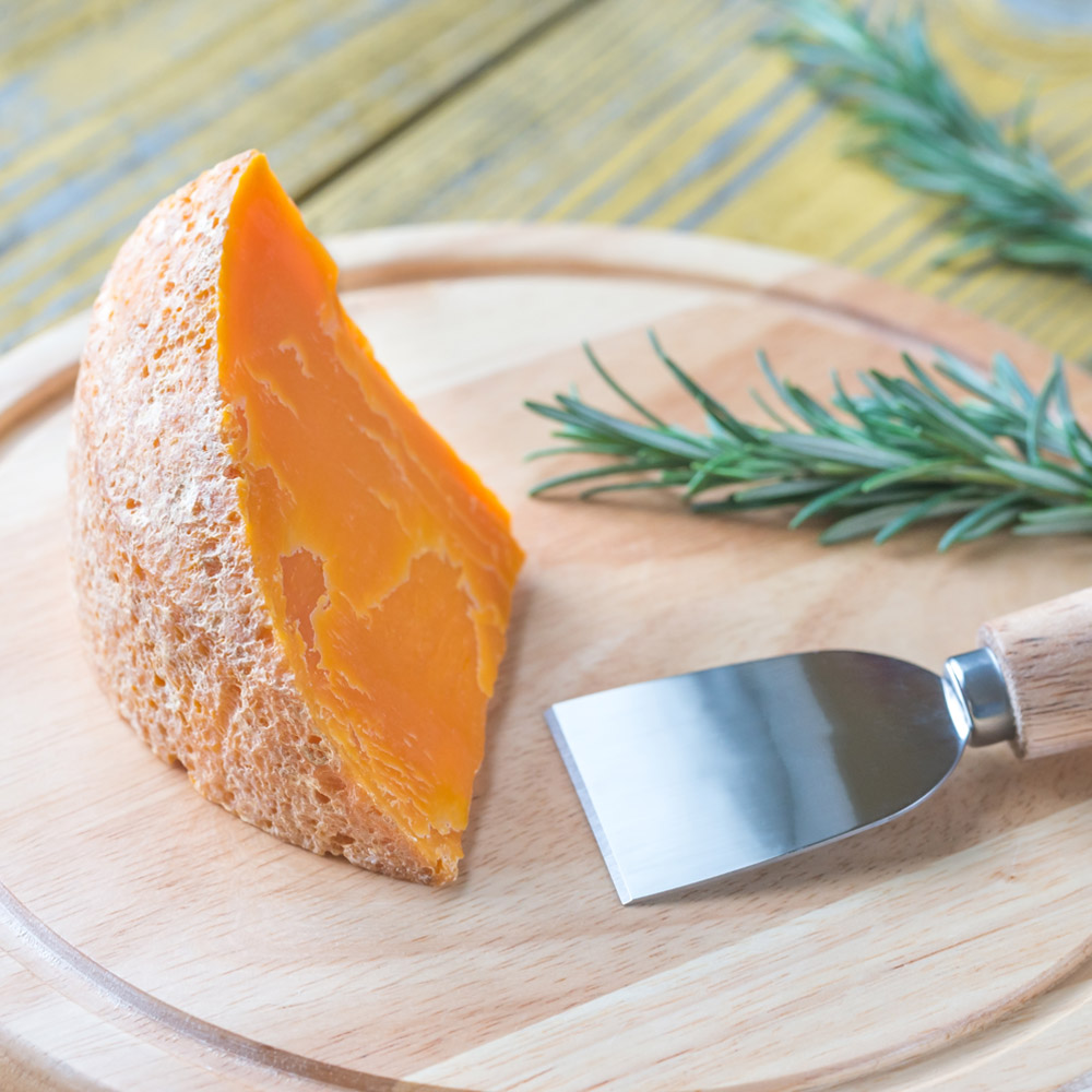 A piece of Mimolette cheese on a wood board with a cheese knife