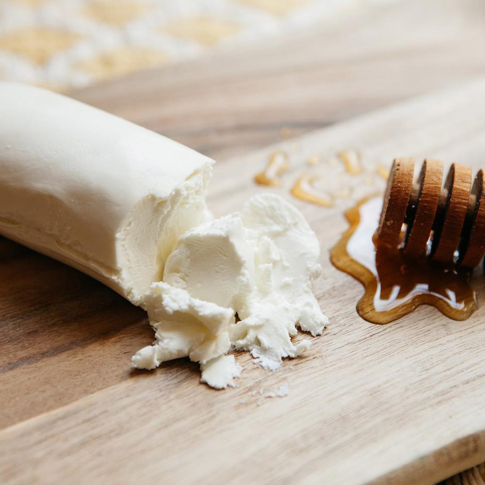 Mackenzie Creamery honey chèvre log on a wood board next to a puddle of honey and a honey dipper
