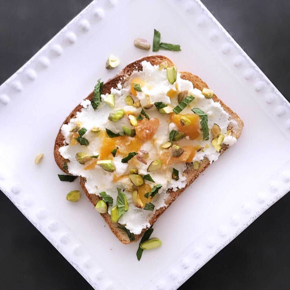 A piece of toast topped with chevre, fruit, and seeds on a plate