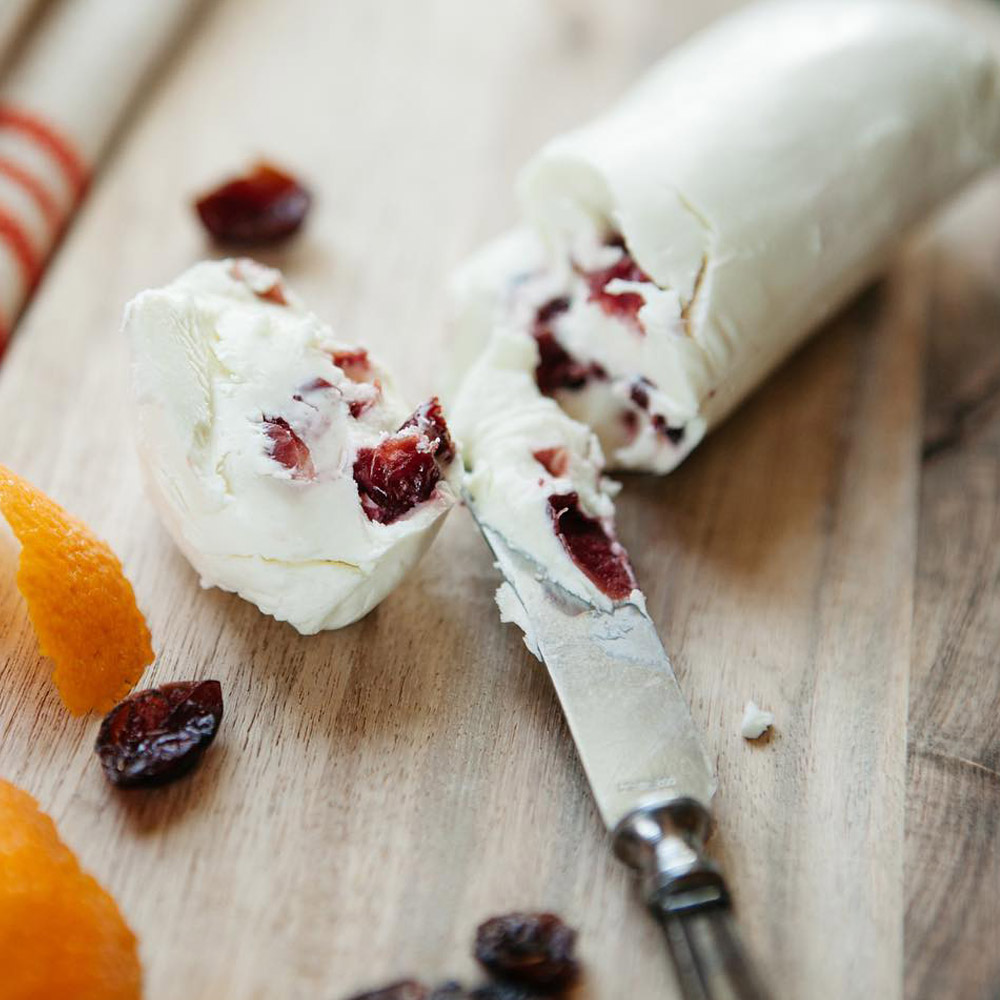 Mackenzie Creamery cranberry orange chèvre log on a wood board with a cheese knife and orange peel