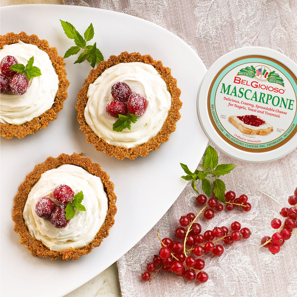 Three mascarpone tarts on a plate next to a container of BelGioioso mascarpone and some red berries