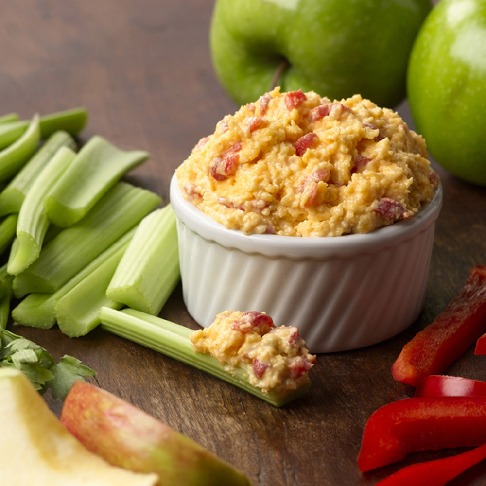 Bowl of pimento cheese next to celery and apples