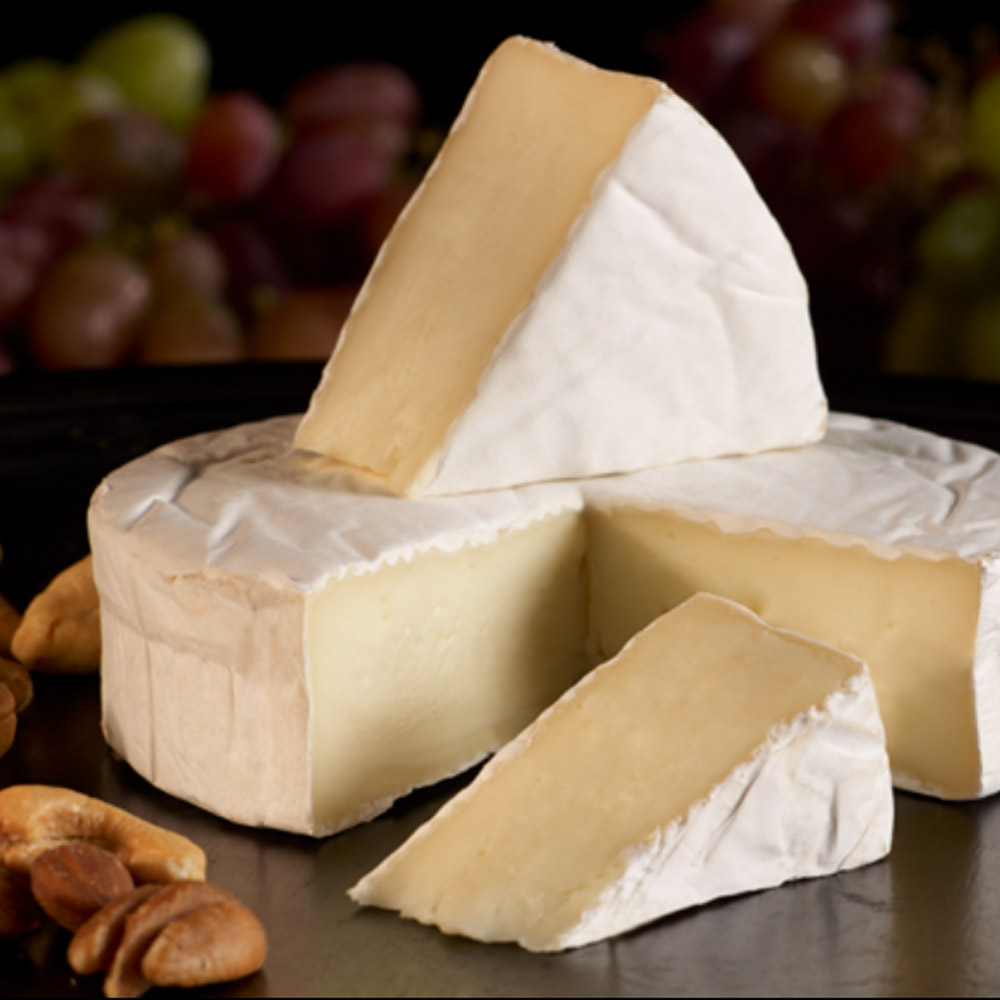 Reny Picot double crème brie with a wedge cut out next to nuts with grapes in the background