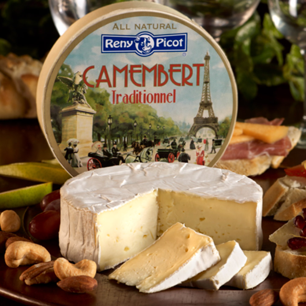 Wheel of Reny Picot double crème Camembert cut with wedges missing in front of packaging surrounded by nuts