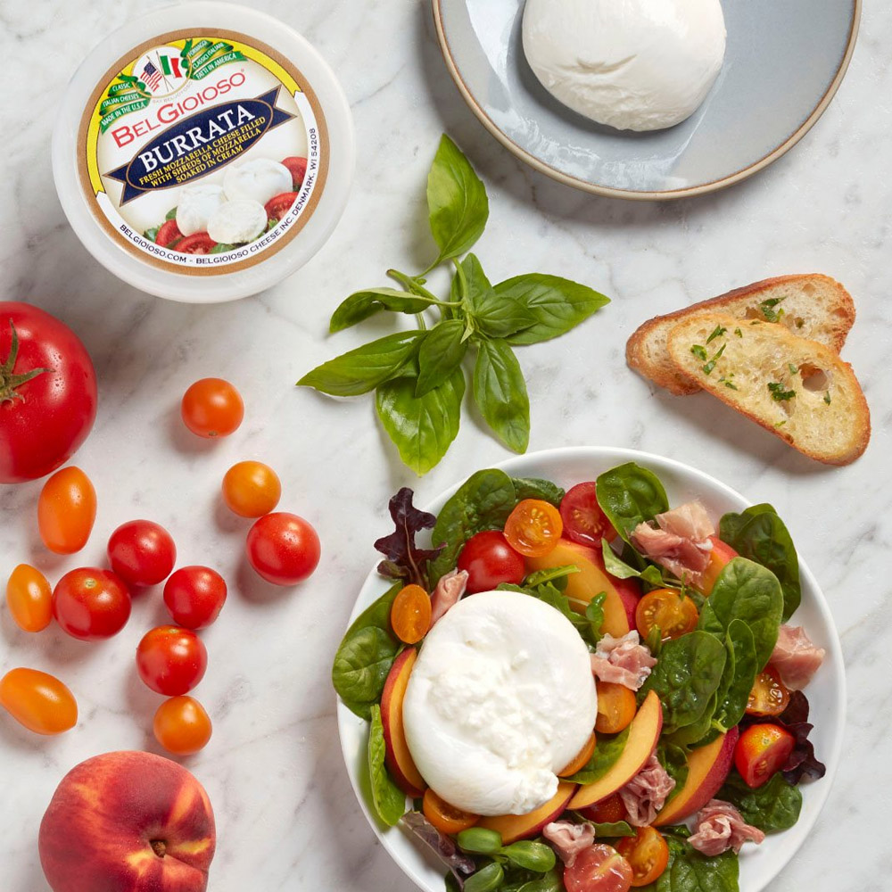Container of BelGioioso Burrata next to a salad with burrata and a couple pieces of bread
