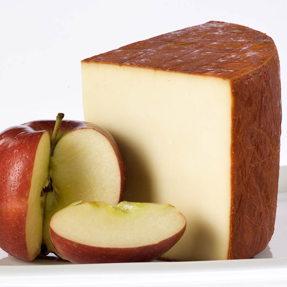 A wedge of Carr Valley Apple Smoked Cheddar on a plate next to a cut apple