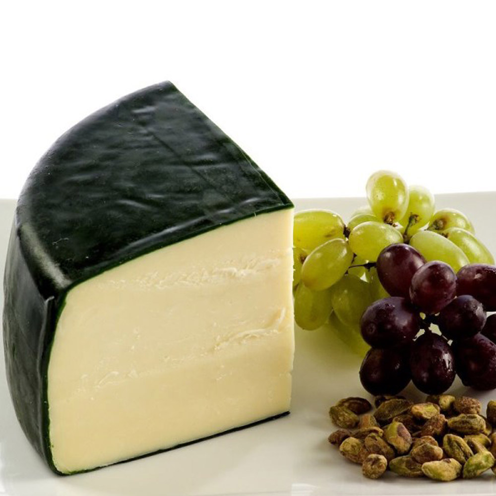 A wedge of Carr Valley Menage cheese on a plate with grapes and pistachios