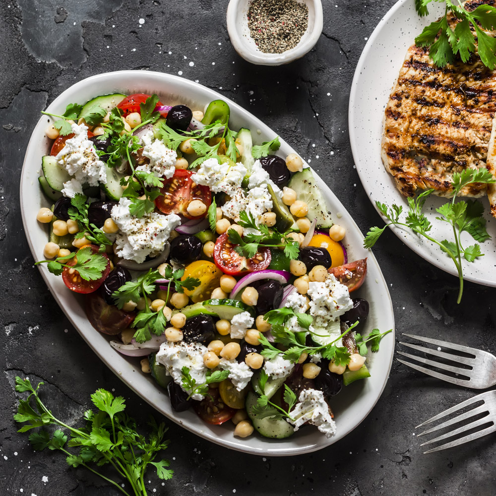 A large Mediterranean style salad topped with feta cheese next to a plate of grilled pork chops