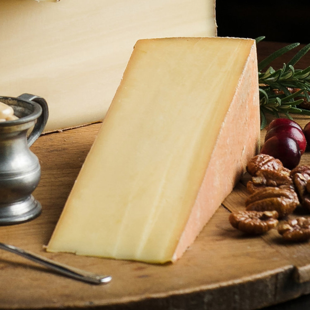 A wedge of cheese on a wood board next to nuts and cherries