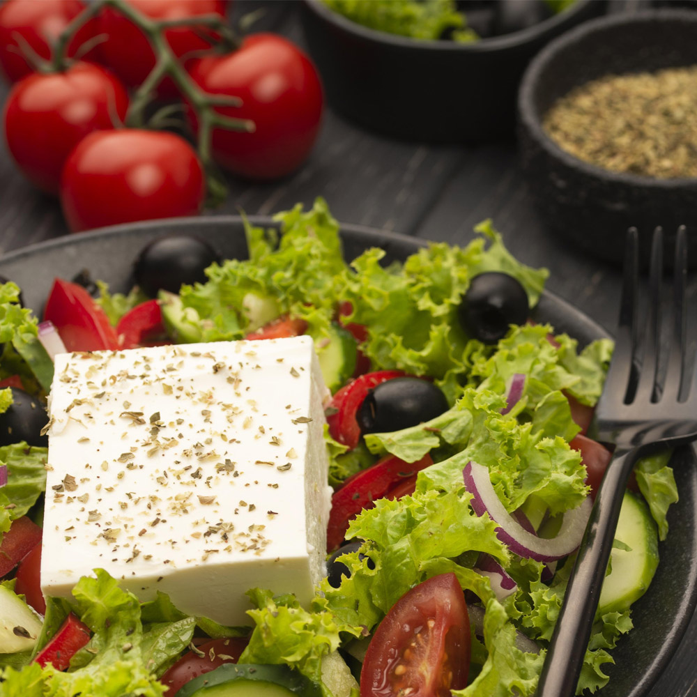 A chunk of feta cheese on top of a salad sprinkled with herbs