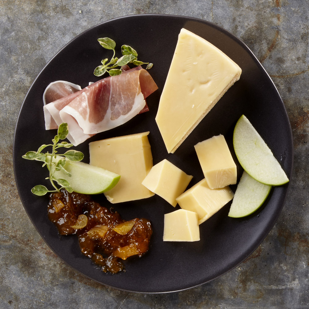 A wedge of gouda on a plate with accompaniments