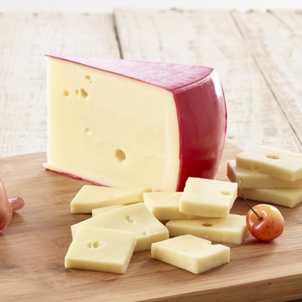 A wedge of fontina on a cutting board next to smaller pieces of fontina cheese and a cherry