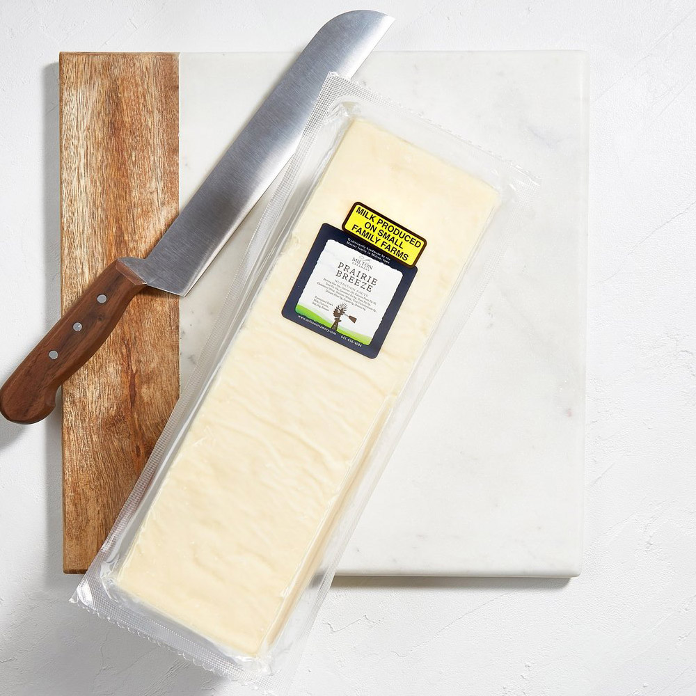 A loaf of Milton Creamery Prairie Breeze Cheddar on a cheese board next to a knife