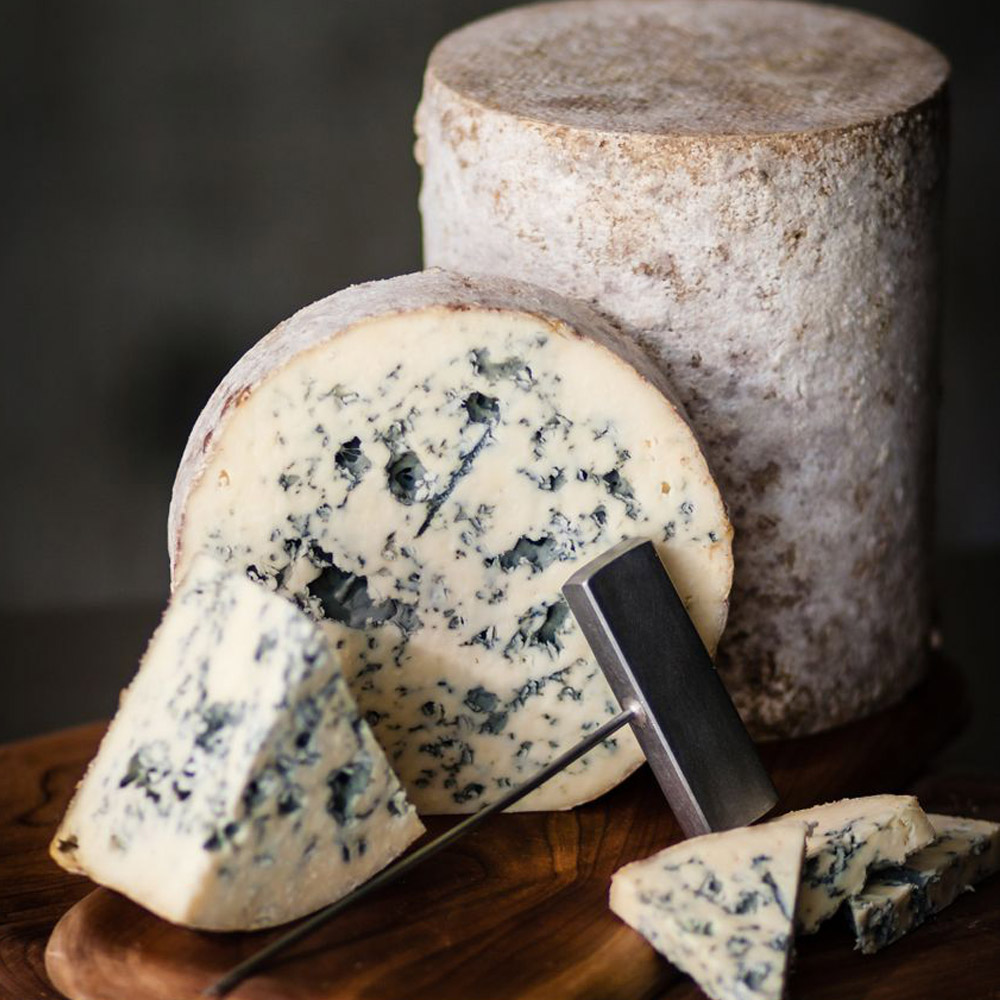 Jasper Hill Bayley Hazen Blue cheese on a wood board with a cheese knife