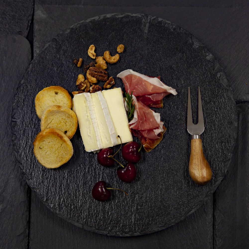 Slices of Old Chatham Creamery Hudson Valley Camembert on a slate board with cherries, nuts, crackers and prosciutto