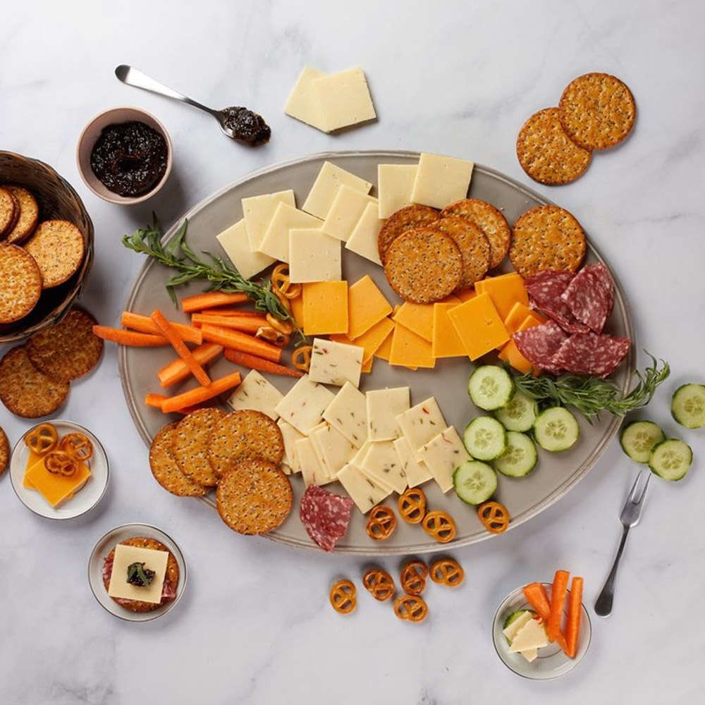 A cheese board with three types of cracker cut cheese and accompaniments