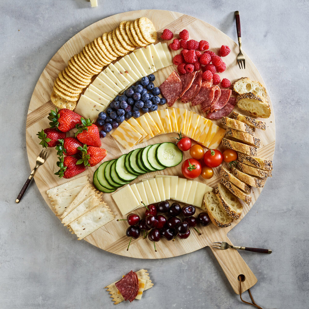 A large round cheese board with three types of cracker cut cheeses and accompaniments