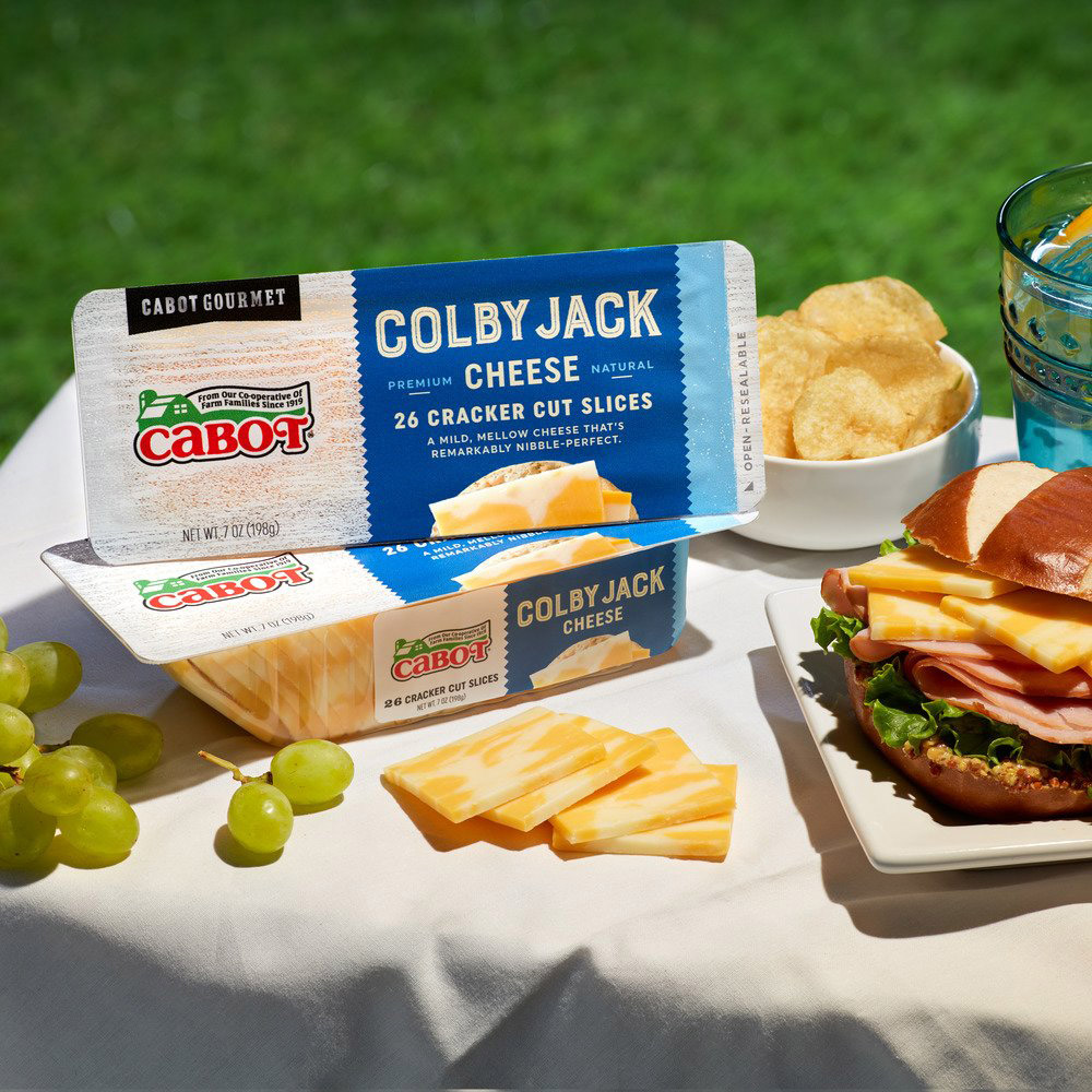 Two packages of Cabot Colby Jack Cracker Cuts on a picnic blanket outside with other snacks