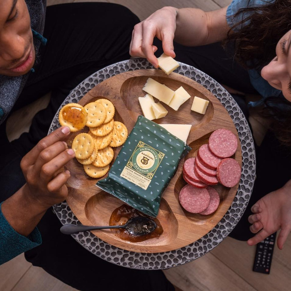 A board with white cheddar, salami, jam and crackers