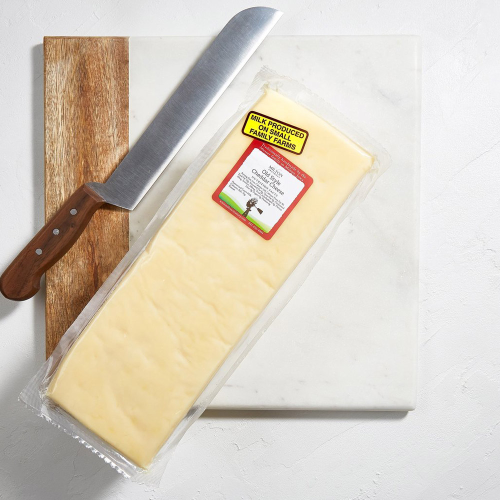 A loaf of Milton Creamery Old Style Cheddar on a cheese board next to a cheese knife