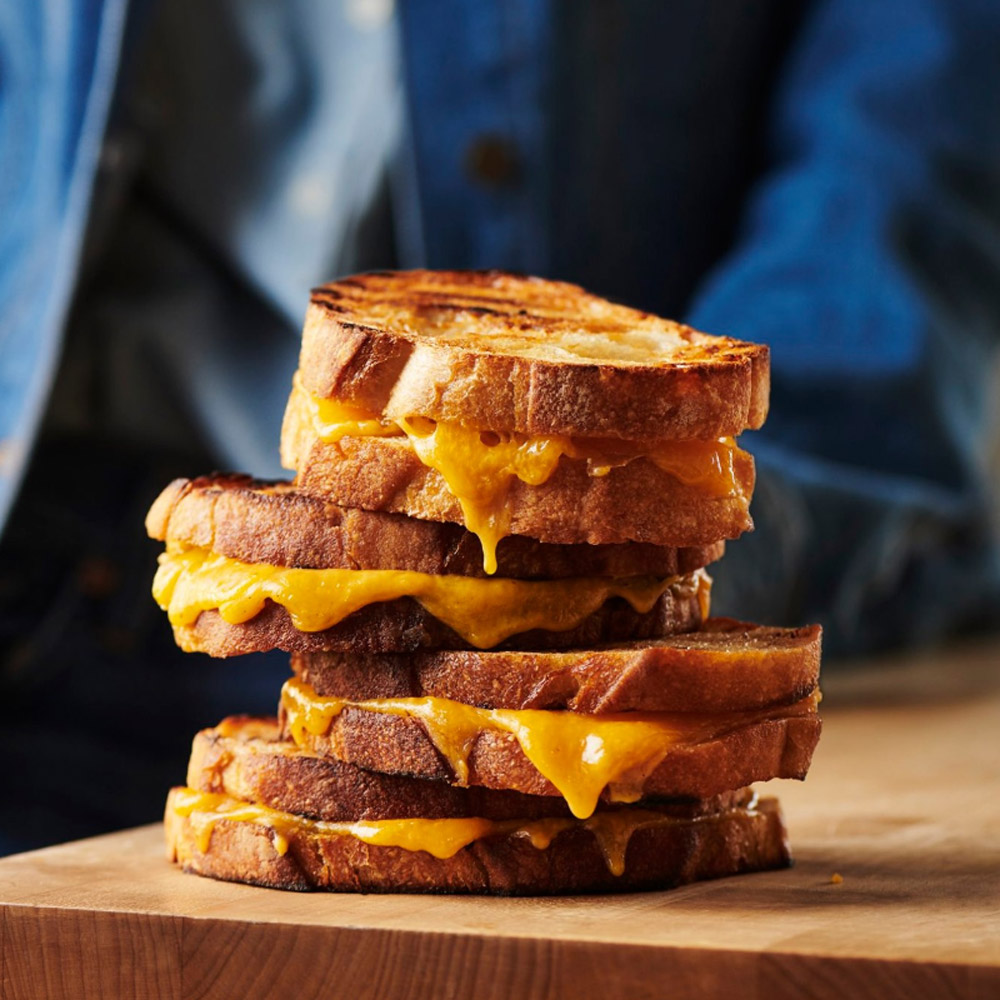 A stack of melty cheddar cheese sandwiches on a wood board