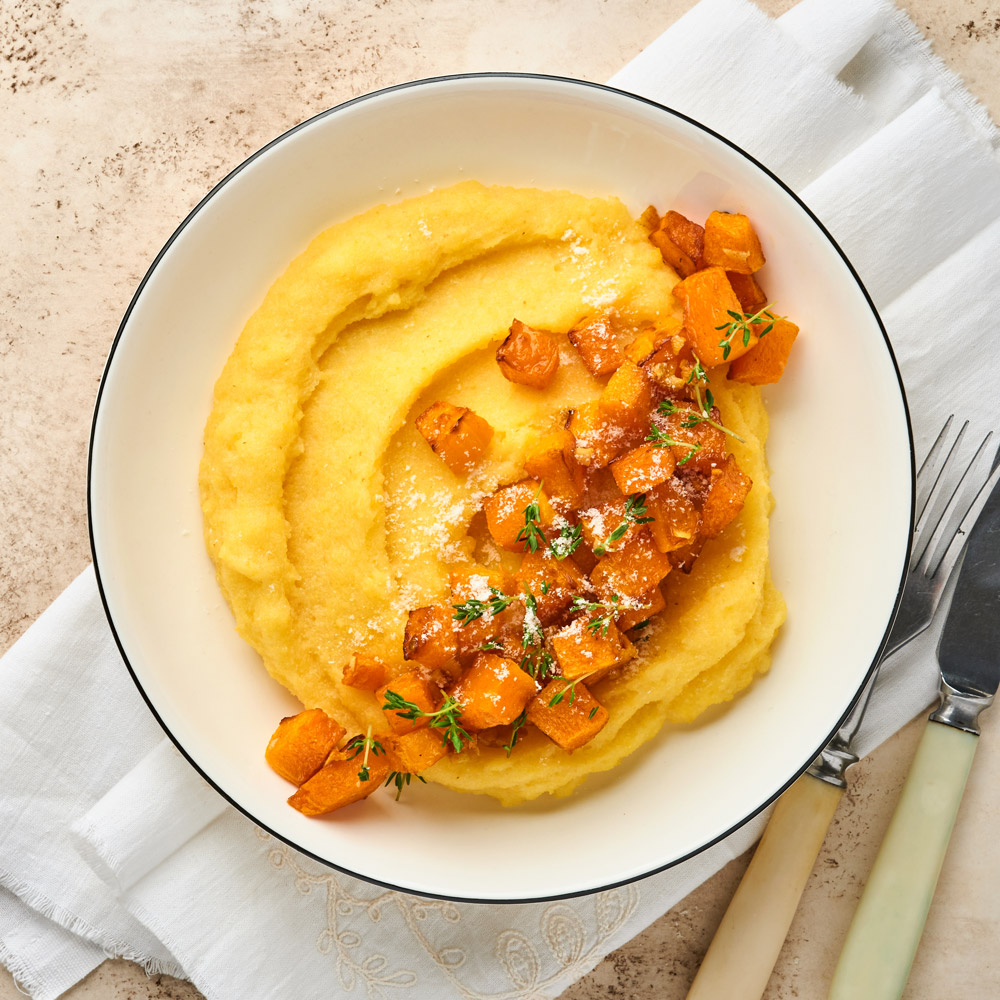 Polenta with butter, pumpkin, garlic, savory and parmesan cheese in white bowl on light concrete background